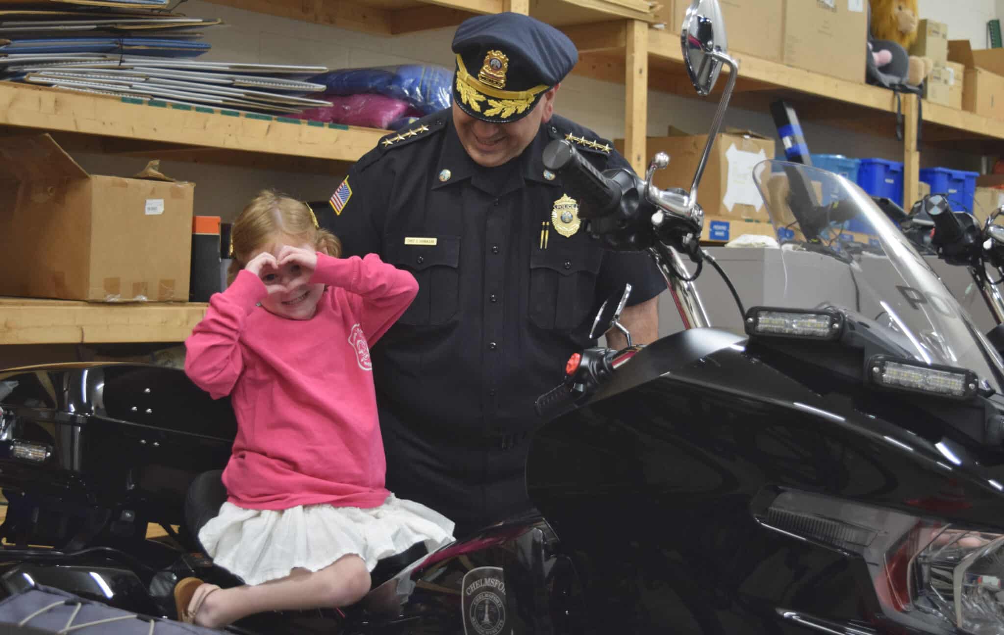 Five-year-old Carson Doherty makes a heart with her hands after Chelmsford Police Chief Gary Hannagan helped her onto a Chelmsford Police motorcycle at the station.