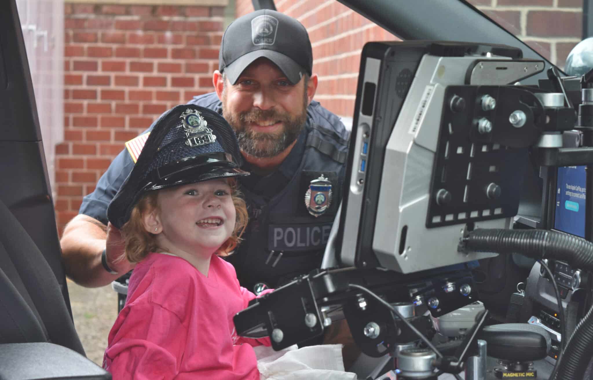 Chelmsford Police Officer Cory D'Entremont stands behind 5-year-old Carson Doherty as she explores a Chelmsford Police cruiser outside of the police station on Thursday.