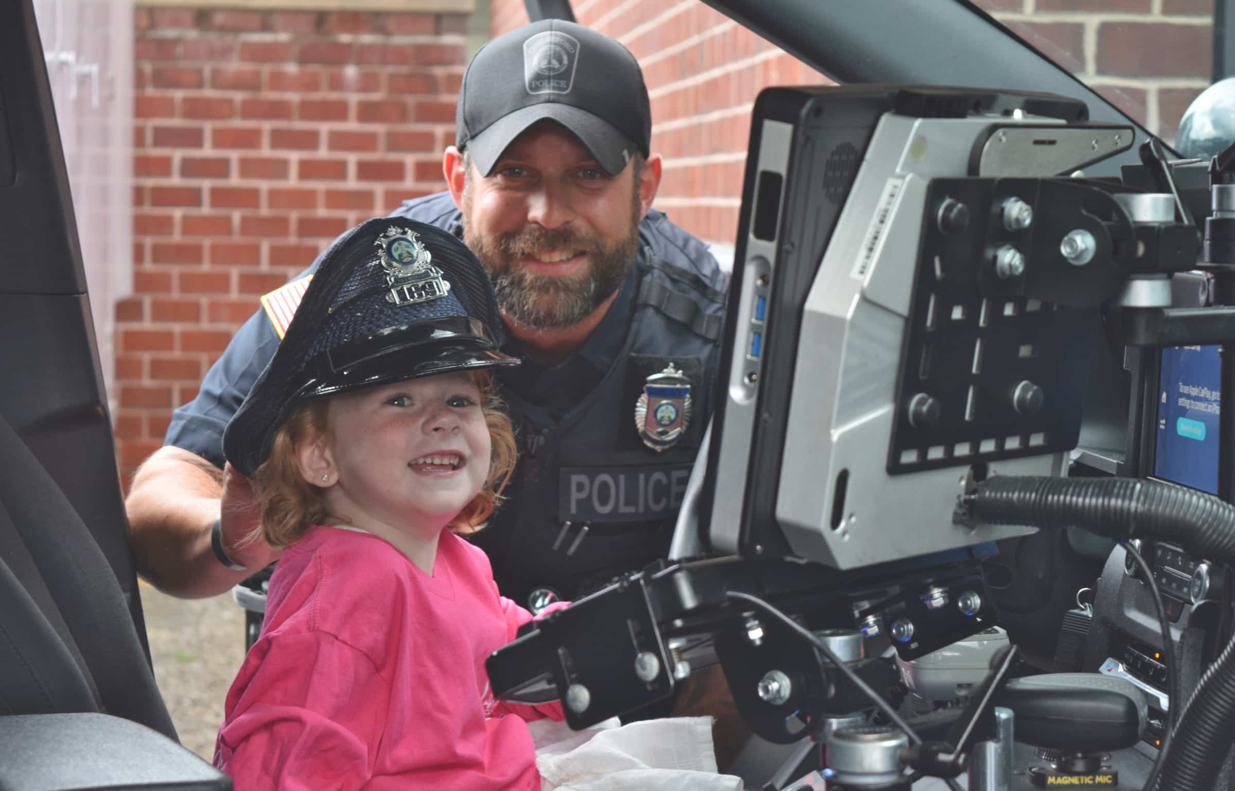 Chelmsford Police Officer Cory D'Entremont stands behind 5-year-old Carson Doherty as she explores a Chelmsford Police cruiser outside of the police station on Thursday.