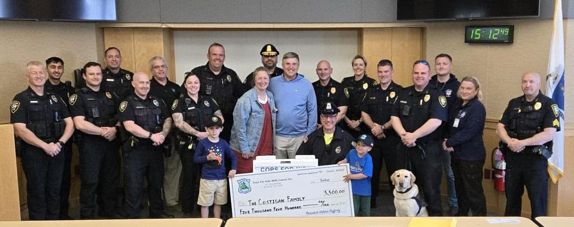 Representatives of Acton Police and Cops for Kids with Cancer stand together with 3-year-old Henry Costigan and his family at the Acton Police Department.