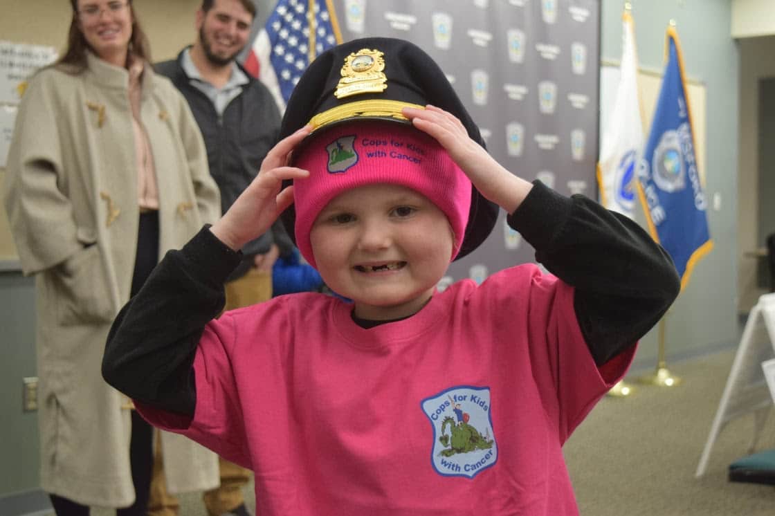 Six-year-old Olivia Kazanjian, who is battling Acute Lymphoblastic Leukemia, tries on a couple new hats while visiting the Chelmsford Police station on Saturday. Cops for Kids with Cancer and Chelmsford Police provided the Kazanjian family with ,500 to support them in their ongoing cancer fight.