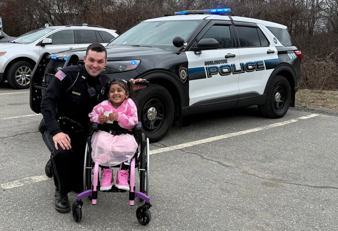 Officer Timothy Pinkham stands with Zoya near a Bulington Police cruiser. Police gave Zoya a tour of the station and several gifts as Cops for Kids with Cance presented Zoya's family with a check to support the family's ongoing battle with cancer.